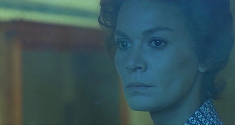 Footprints (Le Orme) (1975) movie still: closeup — A close-up shot focuses on a woman in a dimly lit, blue-toned interior space. She gazes slightly…