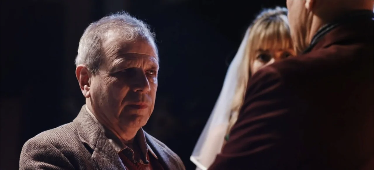 The Russian Bride (2019) movie still: medium — A dimly lit indoor space features two individuals positioned in close proximity. The man in the…