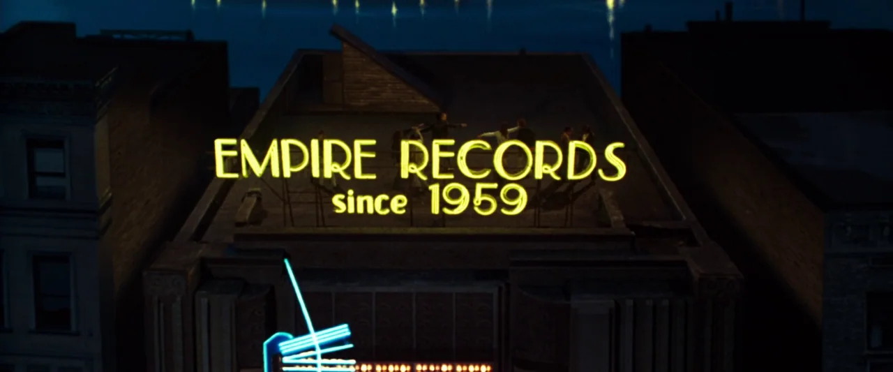 Empire Records (1995) movie still: establishing — A dark city building rooftop features a large glowing neon sign at night. Several small,…