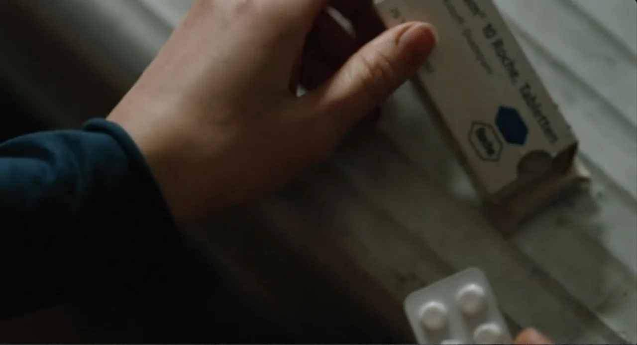Soul Kitchen (2009) movie still: closeup — A close view shows human hands holding a medicine package over a white surface. The person is opening the…