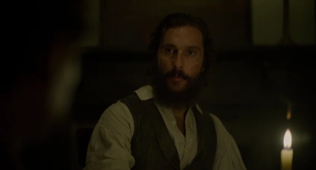 Free State of Jones (2016) movie still: medium — A dim room illuminated by a single candle on a wooden table. A man with a beard sits in the shadows…
