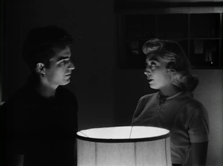 The Killing (1956) movie still: medium — A dark indoor space is illuminated only by a lamp in the foreground. A man and a woman stand facing each…