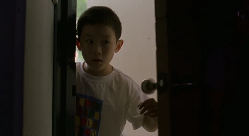 Yi-Yi (A One and A Two) (2000) movie still: medium — A young boy stands in a doorway looking into a dark room. The boy is framed by a heavy wooden…