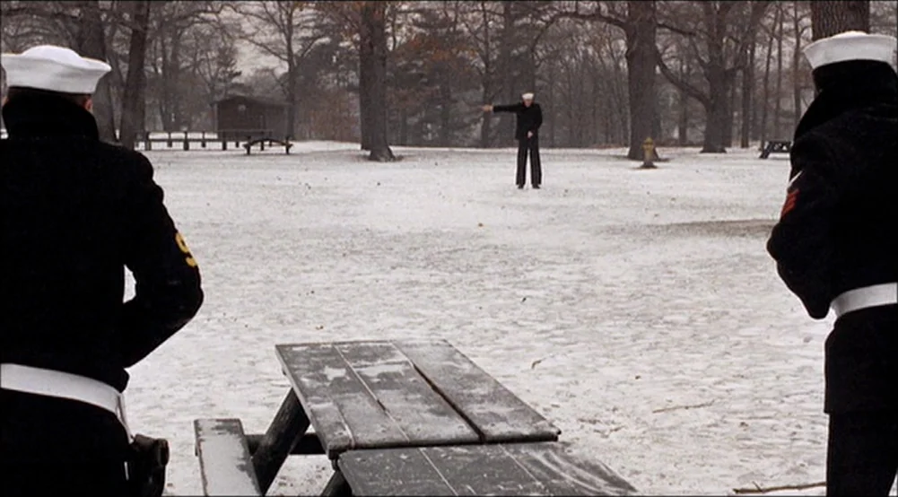 The Last Detail (1973) movie still: wide — A snowy park clearing features a wooden picnic table in the foreground. Three sailors are positioned…