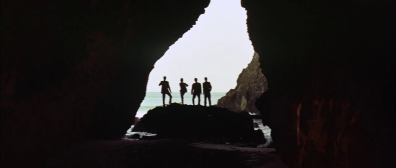 Mothra Vs Godzilla (1964) movie still: wide — The view from inside a dark coastal cave looking toward the bright ocean horizon. Four silhouetted…