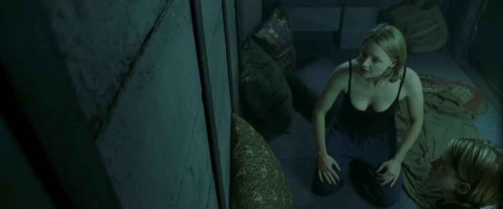 Panic Room (2002) movie still: medium — A confined, dark metallic space with concrete-like walls and several scattered pillows and blankets. An…