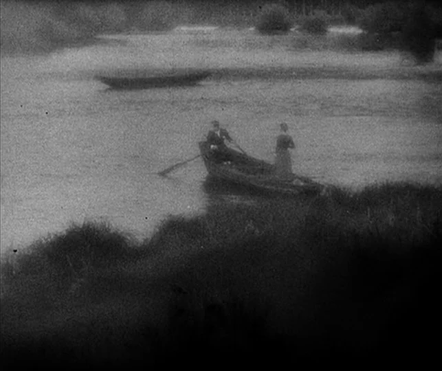 Vampyr (1932) movie still: wide — A wide shot shows a small wooden boat on a river with dark vegetation. A man rows the boat while a woman sits…