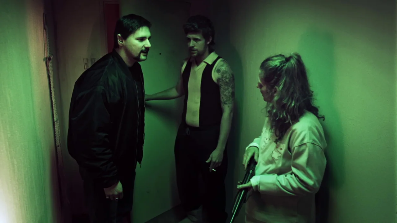 Chopper (2000) movie still: medium — A cramped hallway with drab walls is illuminated by intense green artificial light. Three individuals stand…