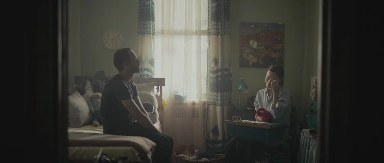 Meadowland (2015) movie still: wide — A cluttered childs room features a single bed and a small desk by window. A man rests on the bed as a woman…