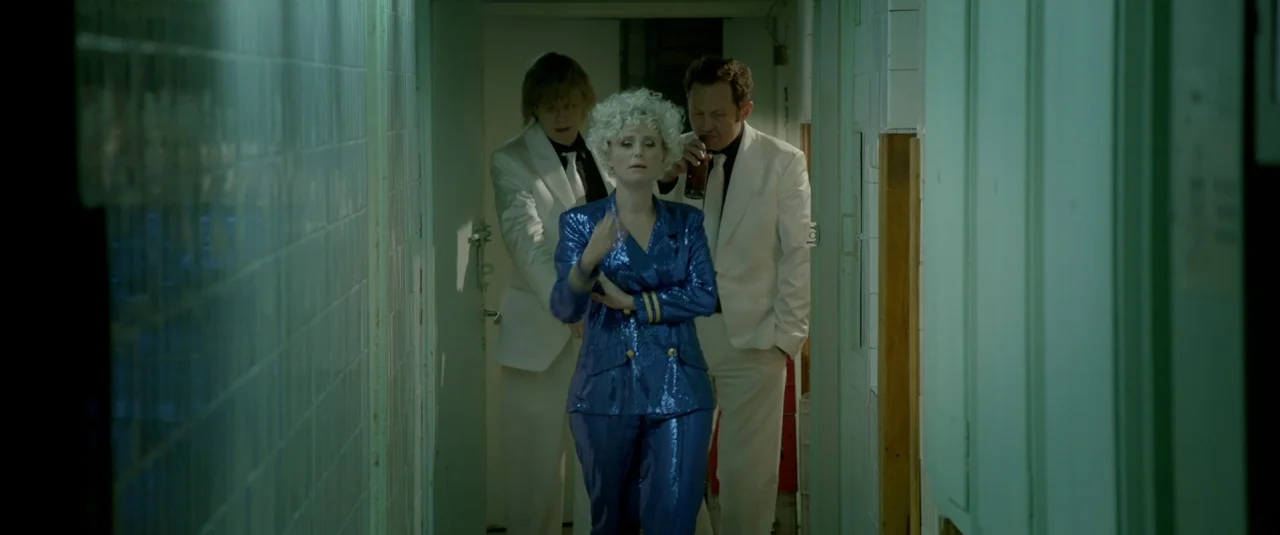 The Lure (2015) movie still: medium — A narrow hospital corridor features pale green tiles on the walls and floor. A woman in a sparkling blue suit…