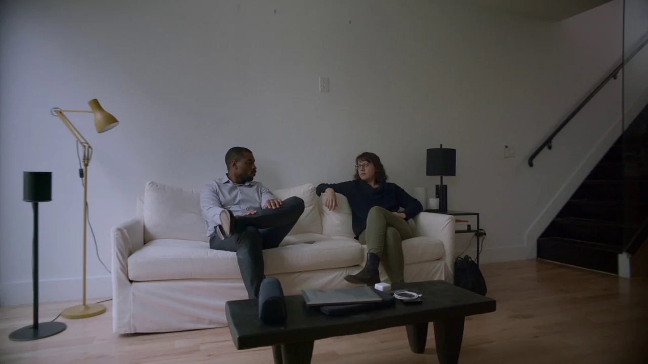 The Feeling That the Time for Doing Something Has Passed (2023) movie still: wide — A minimalist living room features white walls, hardwood floors,…