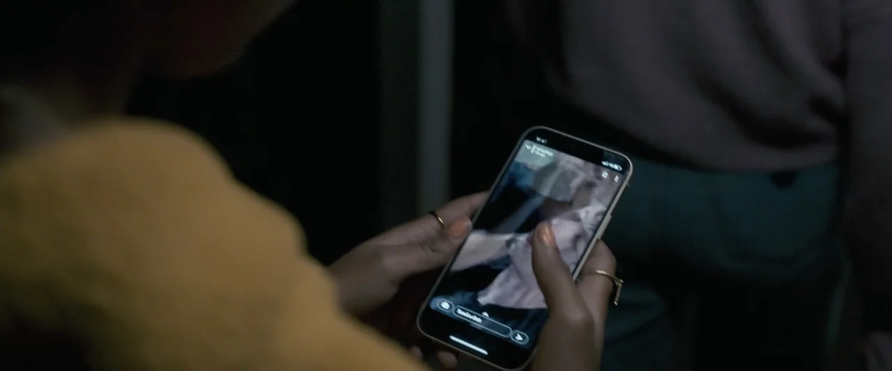 Talk to Me (2023) movie still: closeup — A dim indoor setting features a person holding a smartphone in their hands. The individual observes the…