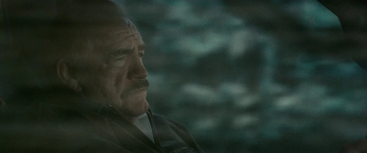 Strange but True (2019) movie still: closeup — An elderly man sits in the dark interior of a car at night. The man stares ahead with a stoic…