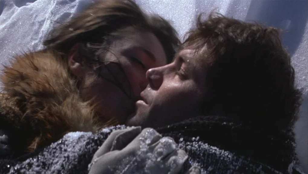 Un Homme et Une Femme (1966) movie still: closeup — A man and woman lie together in a patch of bright, powdery white snow. The pair rest with eyes…