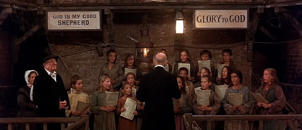 Gangs of New York (2002) movie still: wide — A stone-walled room features two wooden signs reading God Is My Good Shepherd. A conductor leads a…