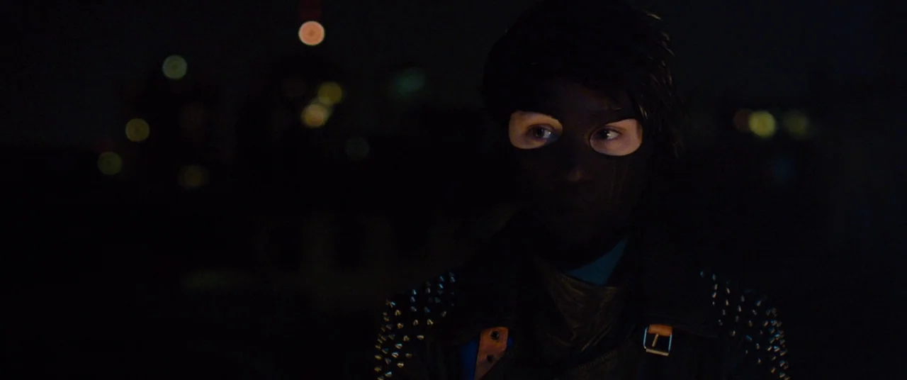 I Origins (2014) movie still: closeup — A person wears a dark mask and a studded leather jacket on a rooftop. The background is a dark cityscape…