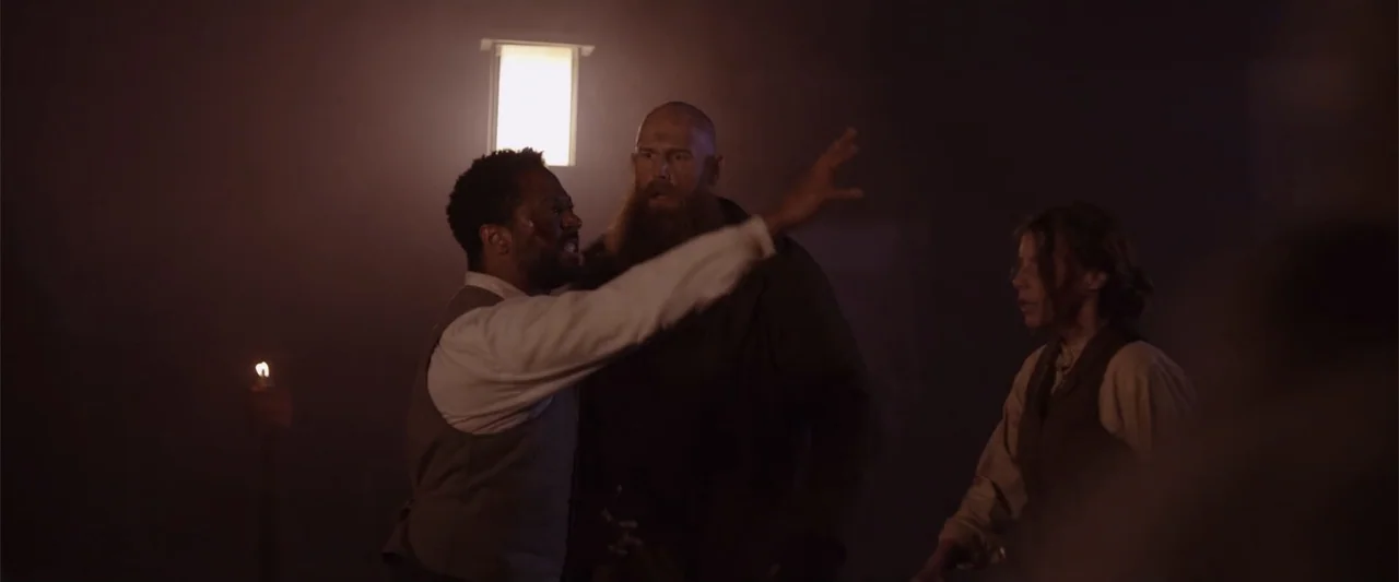 Ghosts of the Ozarks (2022) movie still: medium — A dark indoor space contains three people standing in a hazy atmosphere. The man on the left…