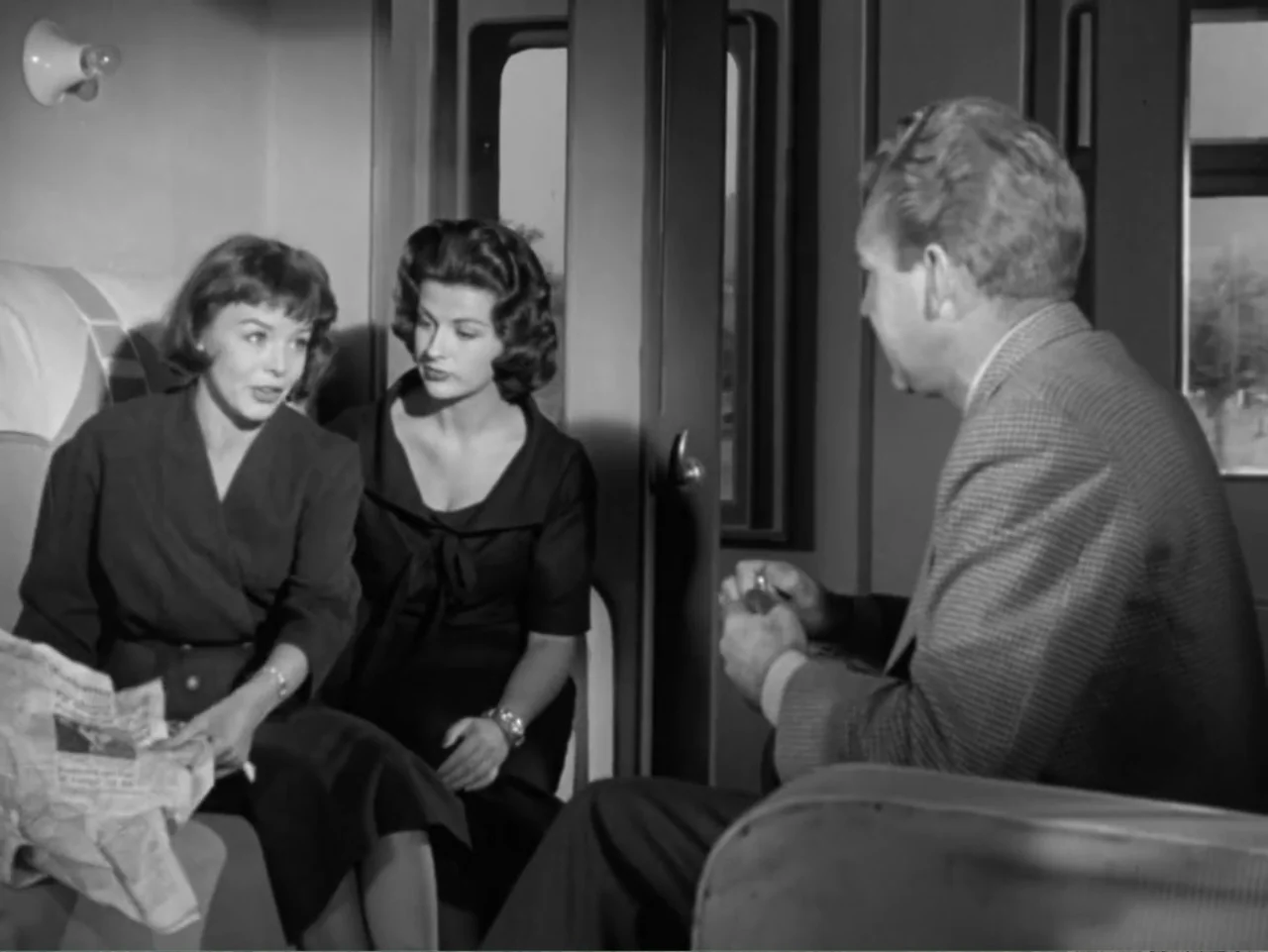 The Crawling Eye (1958) movie still: medium — A 1950s train compartment featuring vinyl seats and framed windows. Two women and a man are seated and…
