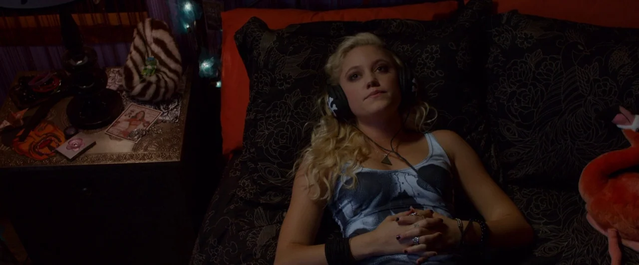 The Guest (2014) movie still: medium — A dark bedroom with patterned dark bedding and a bedside table displaying various trinkets. A young blonde…