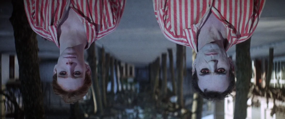 Papillon (1973) movie still: medium — A dark, tree-lined outdoor corridor at night with two men appearing upside down. They both wear identical red…