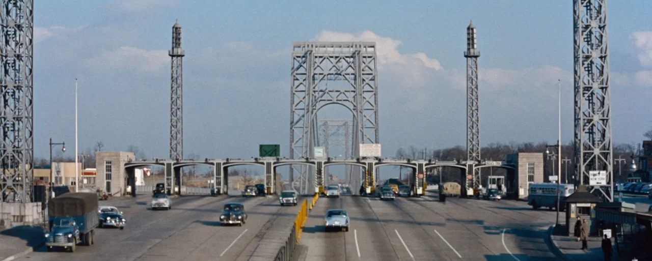 How to Marry a Millionaire movie still: wide — A 1950s toll plaza sits before a massive suspension bridge with tall steel towers. Multiple vintage…