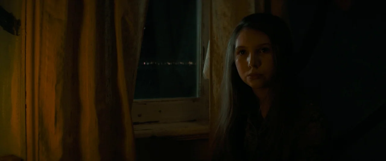 Don’t Breathe 2 (2021) movie still: medium — A dimly lit room at night with thick curtains framing a dark window pane. A teenage girl sits quietly…