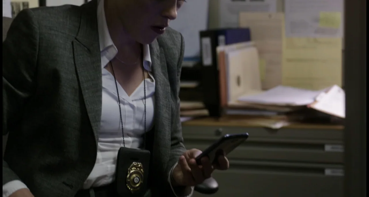 Sabotage (2014) movie still: medium — An indoor workspace contains metal filing cabinets stacked with paperwork and folders. A woman in a grey suit…