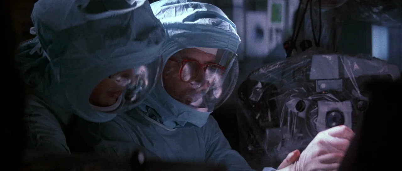 The Adventures of Buckaroo Banzai Across the 8th Dimension (1984) movie still: medium — Two individuals wearing full-body containment gear work in a…