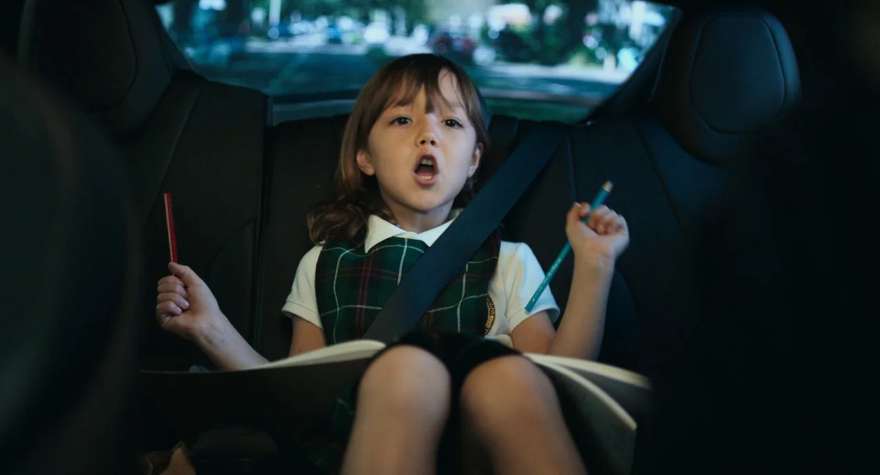 Deep Water (2022) movie still: medium — The interior of a car features black leather upholstery and a rear passenger. A young girl sits buckled in…