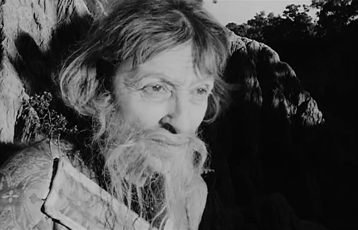 Fando y Lis (1968) movie still: closeup — A rugged outdoor environment features jagged rock formations and distant sparse trees. An older man with a…