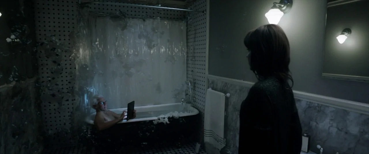 Malignant (2021) movie still: medium — A dark, marble-tiled space with a claw-foot tub draped in clear plastic sheeting. An older man lies in the…