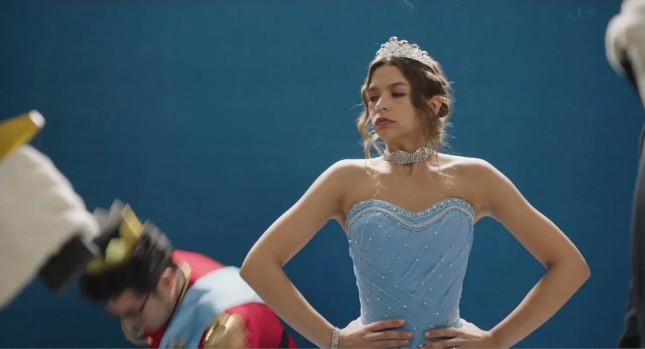 Casando a mi Ex (2023) movie still: medium — A studio setting with a solid dark blue wall in the background. A girl in a blue pageant-style dress…