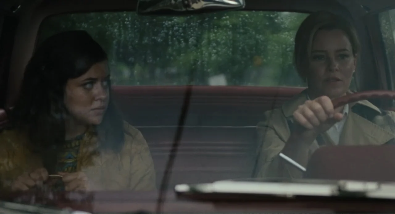 Call Jane (2022) movie still: medium — Inside a moving vehicle during a rainy day with water drops on the glass. The driver maintains focus on the…