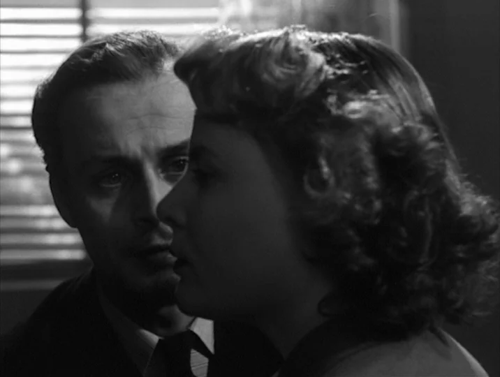 Thirst (1949) movie still: medium — A dark office setting with horizontal window blinds casting light stripes on the background. A man stands behind…