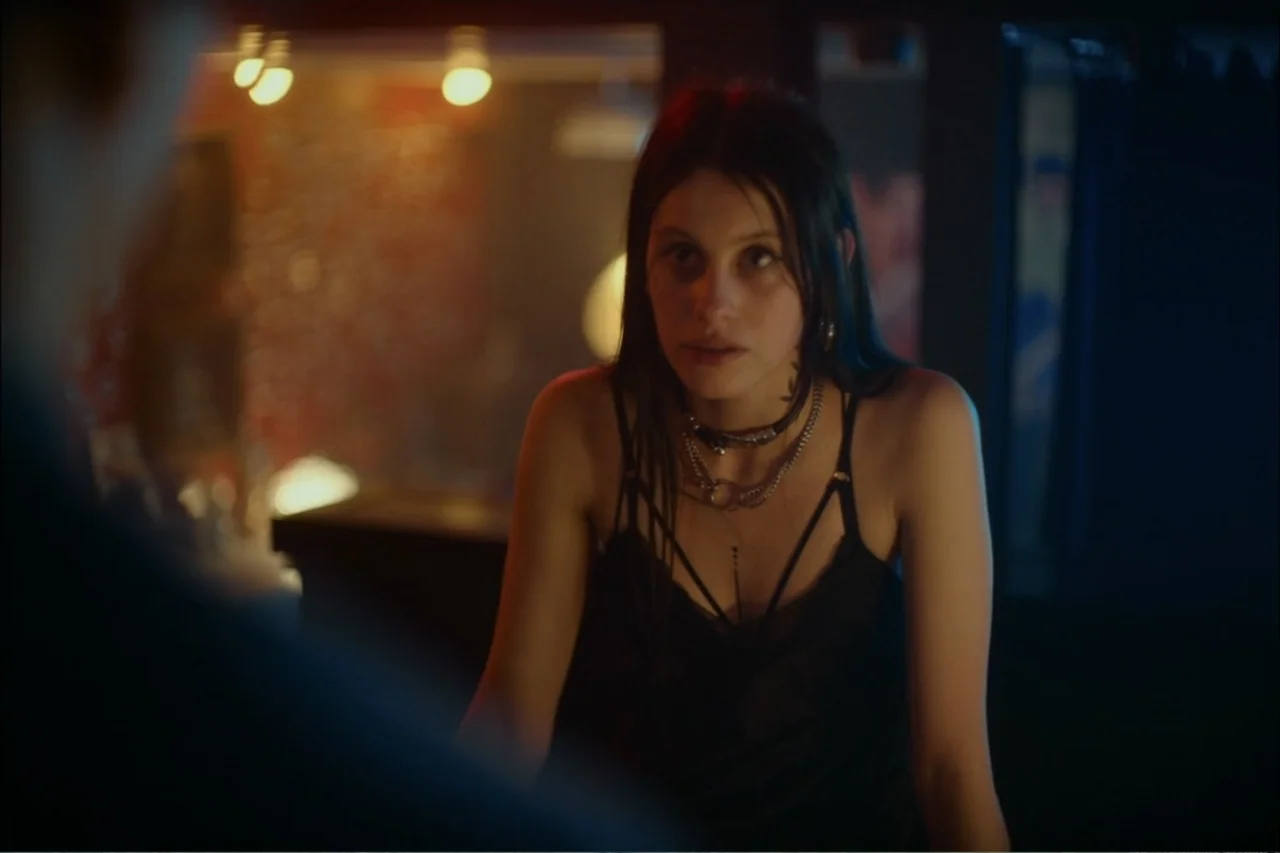 Cross the Line (2020) movie still: medium — A dimly lit bar interior featuring soft background glows from warm practical lamps. A young woman with…