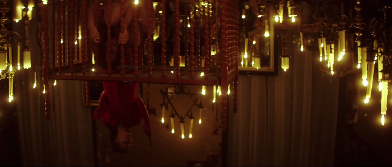Braid (2018) movie still: medium — A dark space filled with numerous candles suspended from the ceiling and around the subject. A woman in a red…