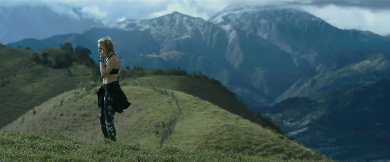 Arthur the King (2024) movie still: fullbody — A woman stands alone on a grassy mountain ridge overlooking a large valley. The subject is in profile…