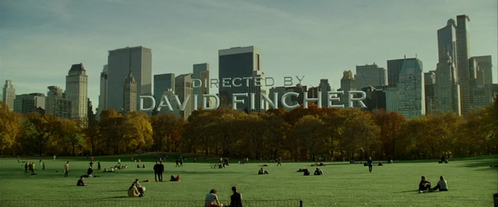 Panic Room (2002) movie still: establishing — A wide view of a city park with a dense skyline in the background. Scattered groups of people occupy…