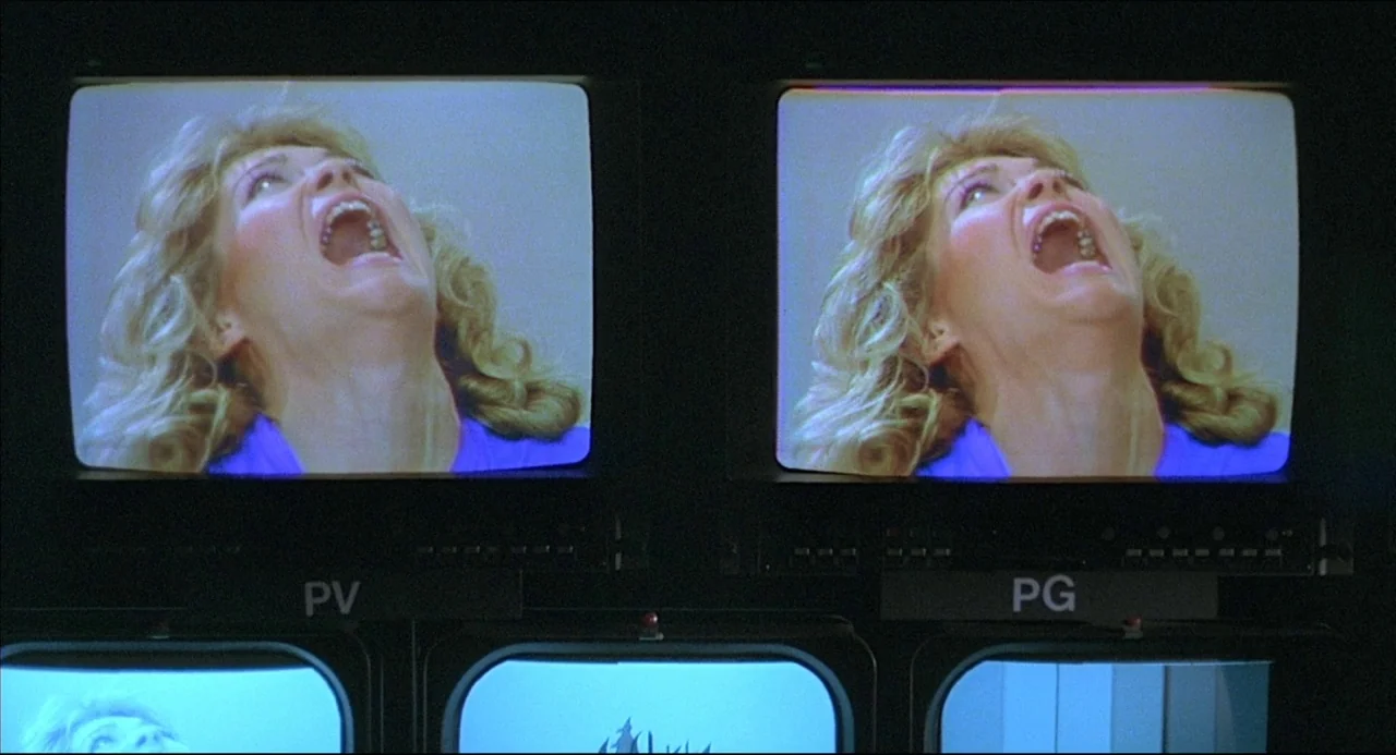 The Howling (1981) movie still: medium — Multiple CRT television monitors in a dark control room display a loop of a woman. The screens are labeled…