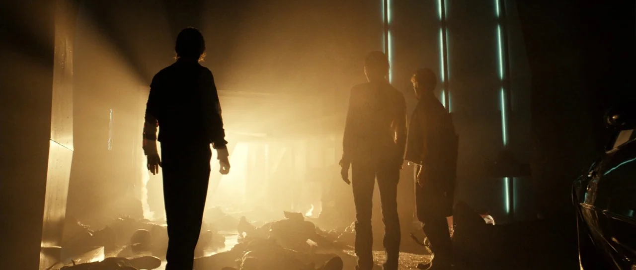 Daybreakers (2009) movie still: wide — An industrial facility interior is filled with heavy debris and thick orange smoke. Three figures stand in…
