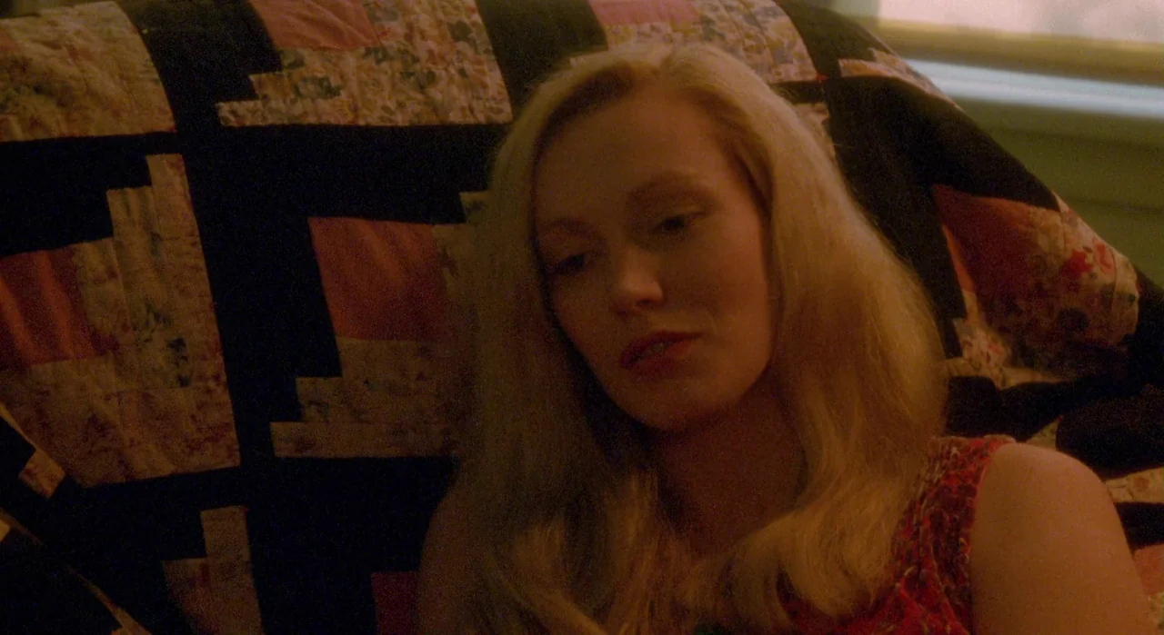 White Of The Eye (1987) movie still: closeup — A woman sits in a home with a patterned fabric quilt visible behind her. She looks down while…