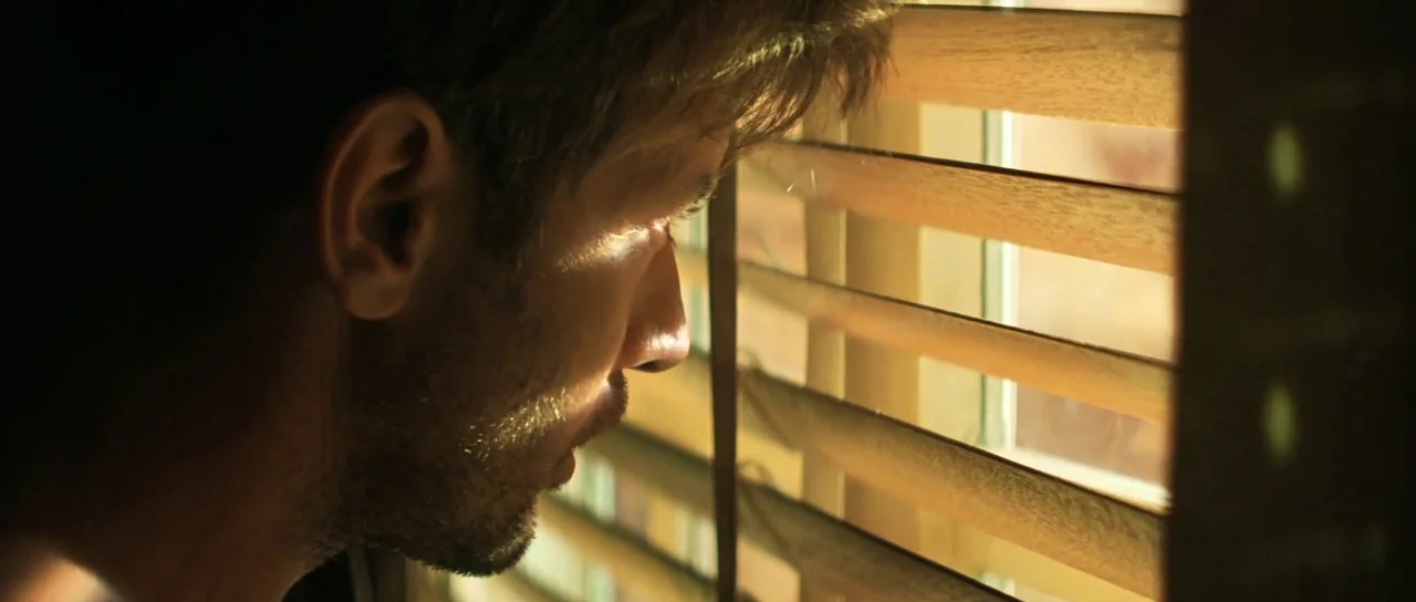 Apocalypse Now (1979) movie still: closeup — A close view shows a man peering through wooden horizontal window blinds. Natural daylight illuminates…