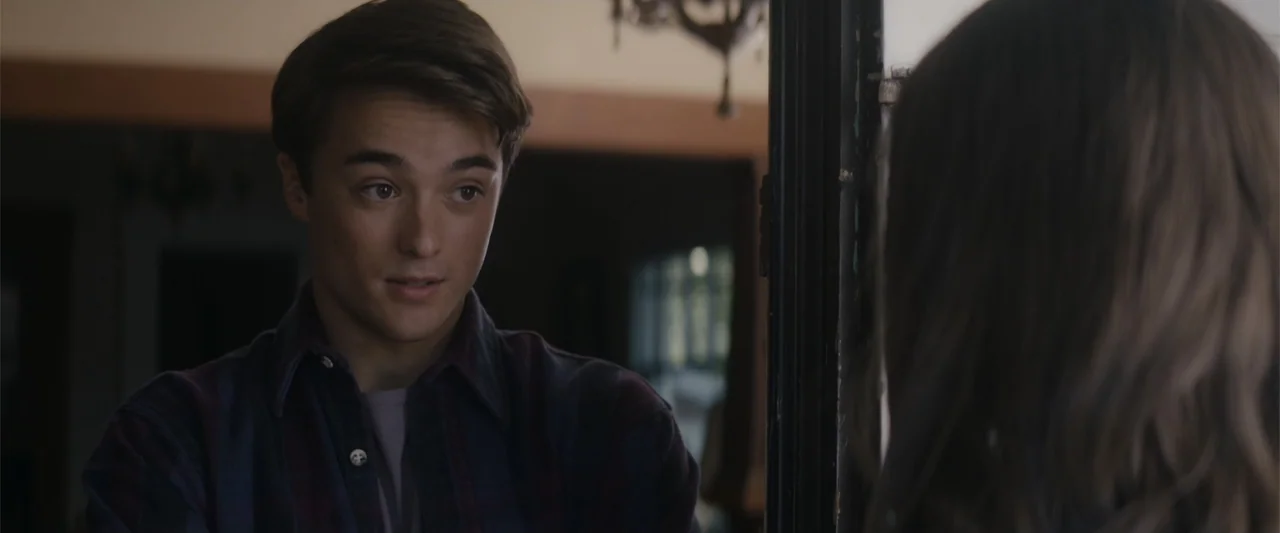 A Christmas Mystery (2022) movie still: medium — A domestic interior with dark furniture and a partially visible window light source. A young man…