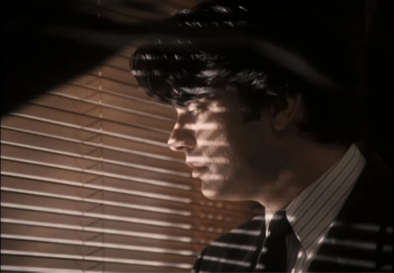 White Mile (1994) movie still: closeup — A man is positioned behind closed horizontal window blinds in an office setting. He stares through the…