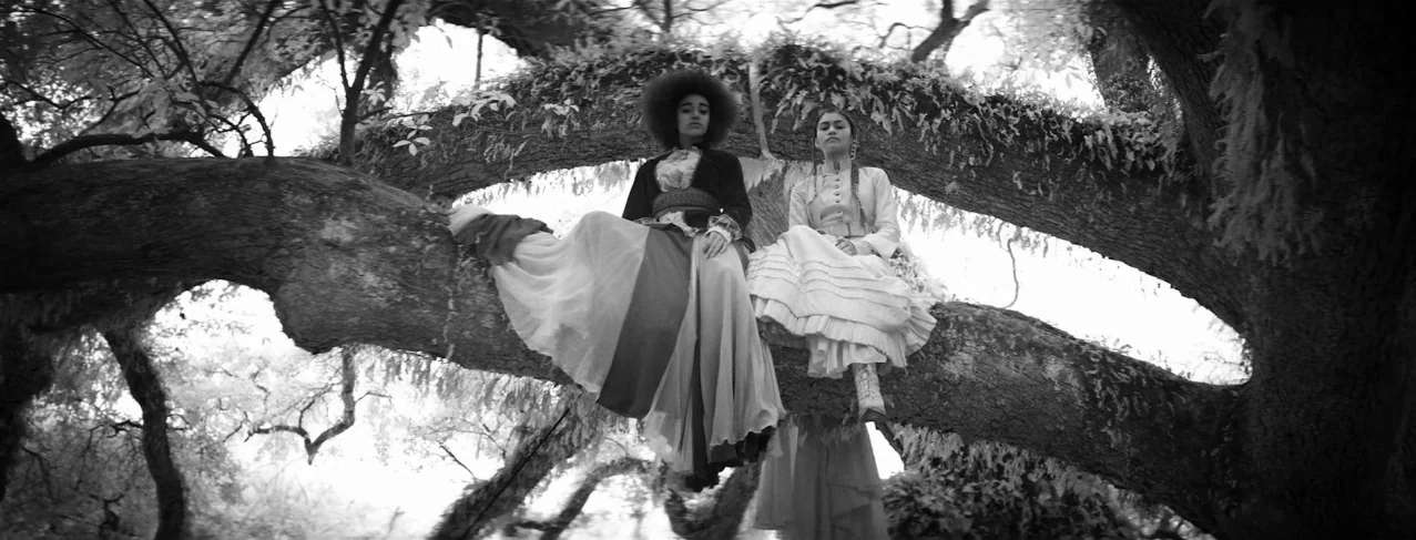 Lemonade (2016) movie still: wide — Two women in historical attire perch on the thick limb of an ancient oak tree. The setting is a bright forest…