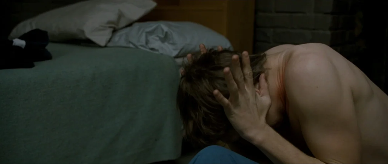 The Haunting in Connecticut (2009) movie still: medium — A dark, sparsely furnished room contains a made bed with rumpled pillows. A shirtless man…