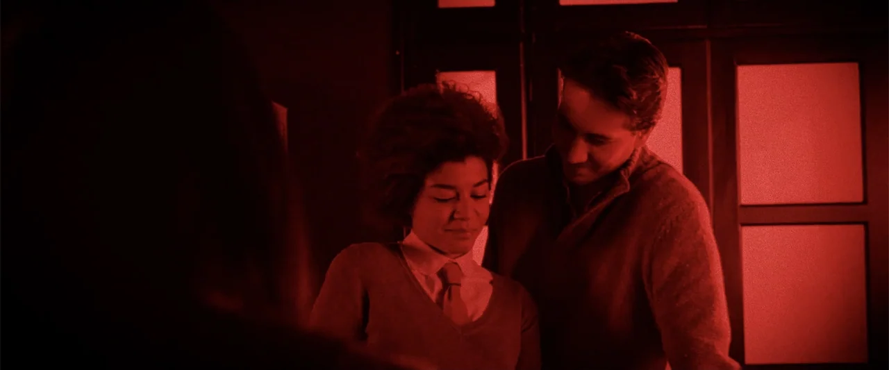 Anna (2013) movie still: medium — A dimly lit indoor space is illuminated by an intense red light source. Two individuals stand close together and…