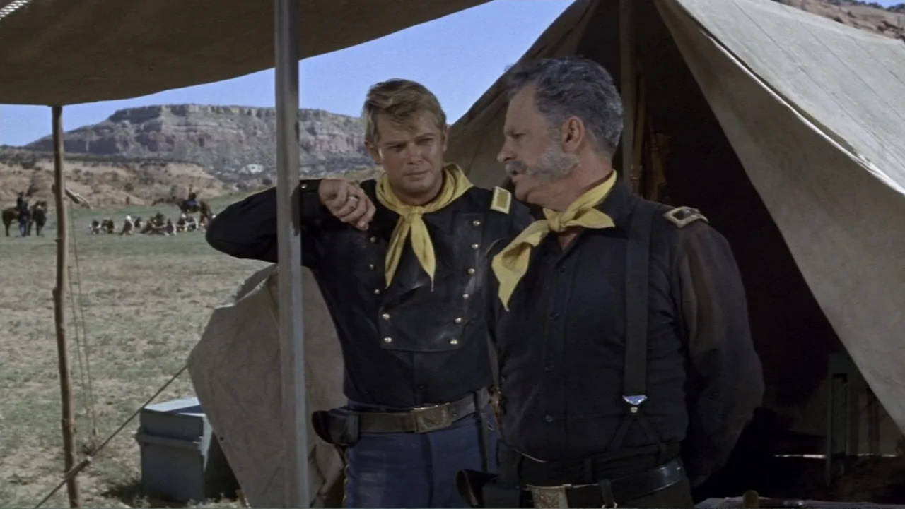 A Distant Trumpet (1964) movie still: medium — A military camp with canvas tents and distant horses in a desert landscape. Two uniformed men stand…