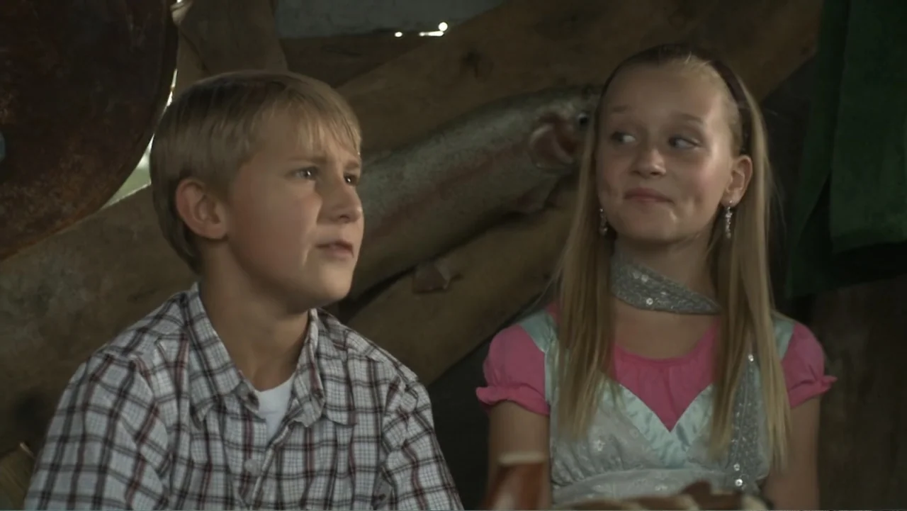Boathouse Detectives (2010) movie still: medium — A rustic interior of a wooden playhouse with rough timber walls. A boy and a girl sit next to each…