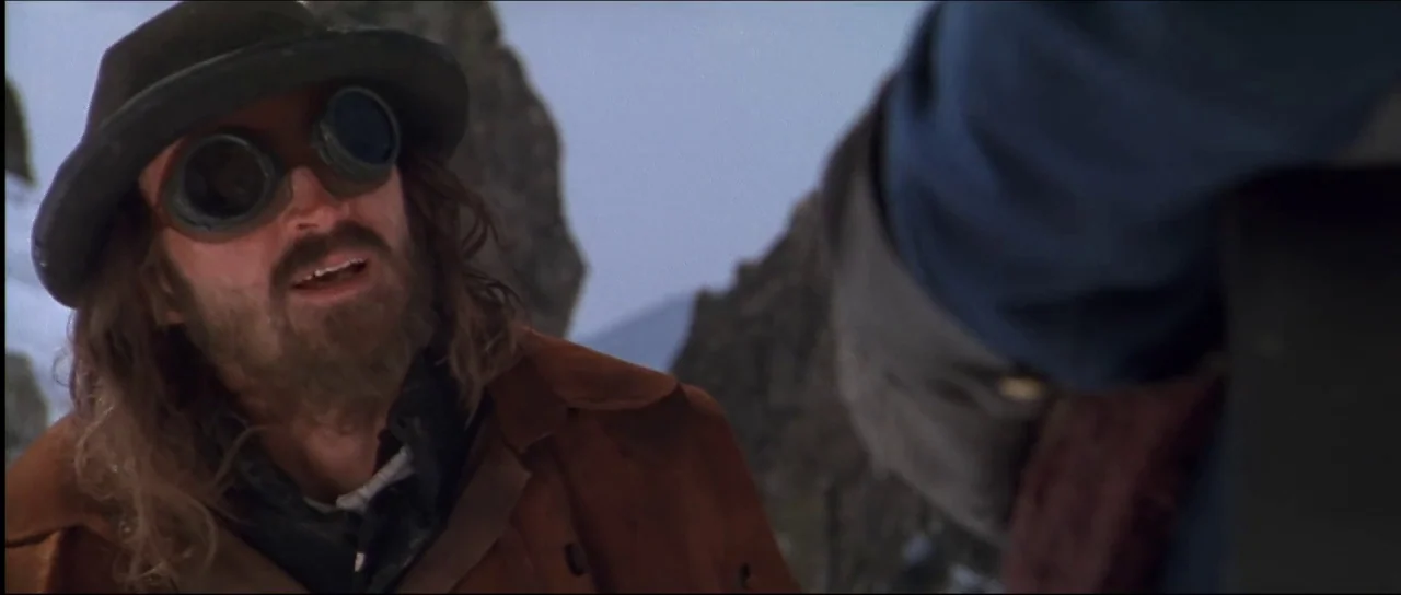 Ravenous (1999) movie still: medium — A rugged mountain landscape with sharp, weathered rock formations against a pale sky. A man wearing leather…